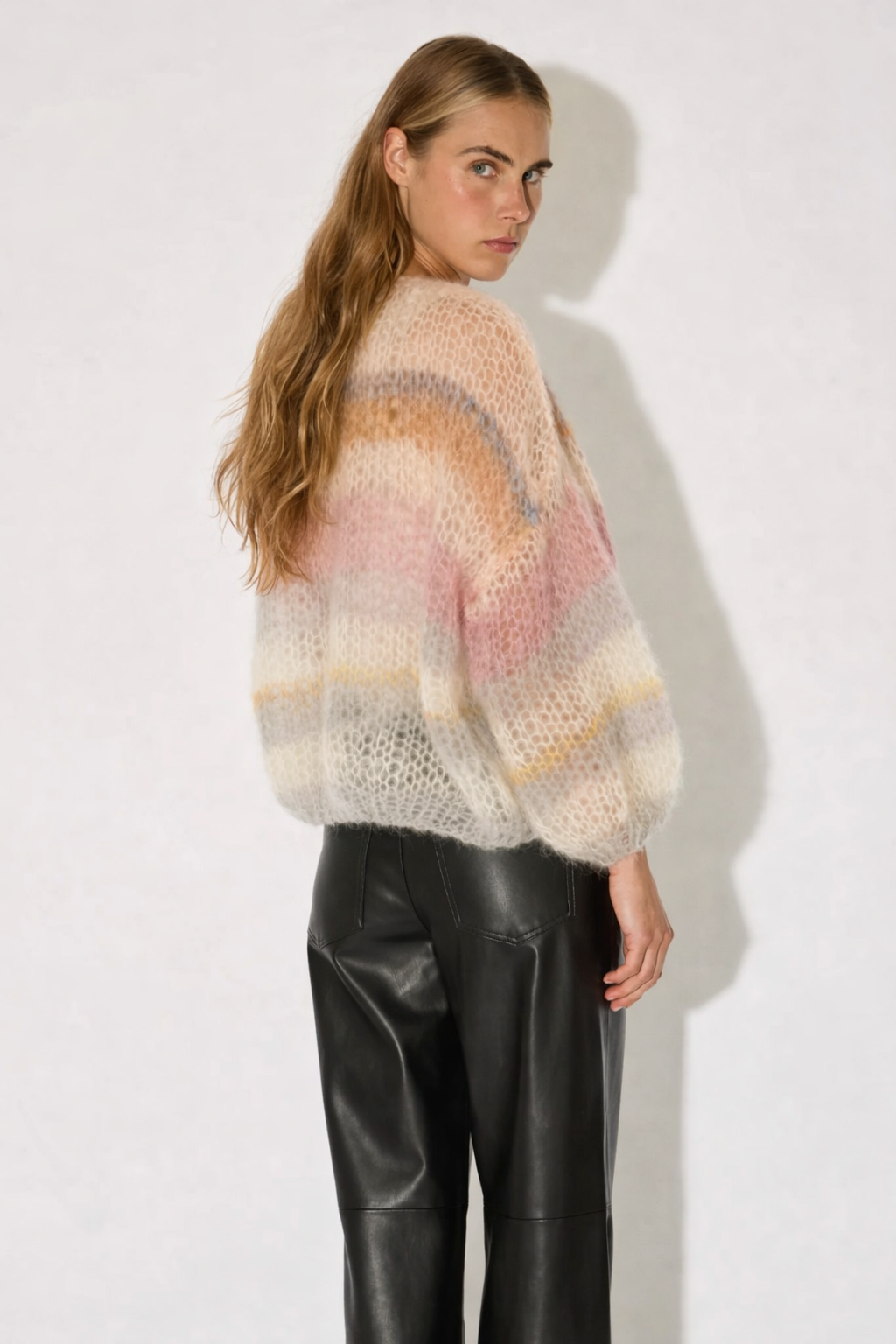 Person wearing a colorful knit sweater and black leather pants on a white background