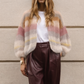Woman wearing a colorful sweater and brown pants against a beige wall