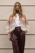 Woman wearing a colorful sweater and brown pants against a beige wall