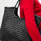Person wearing a red sweater holding a black woven handbag.