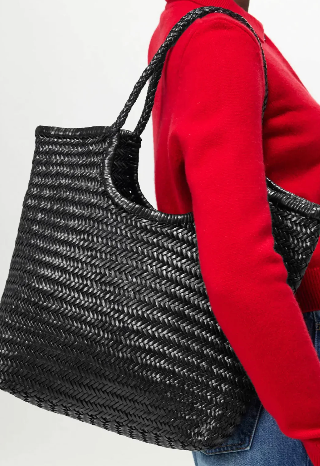 Person wearing a red sweater holding a black woven handbag.