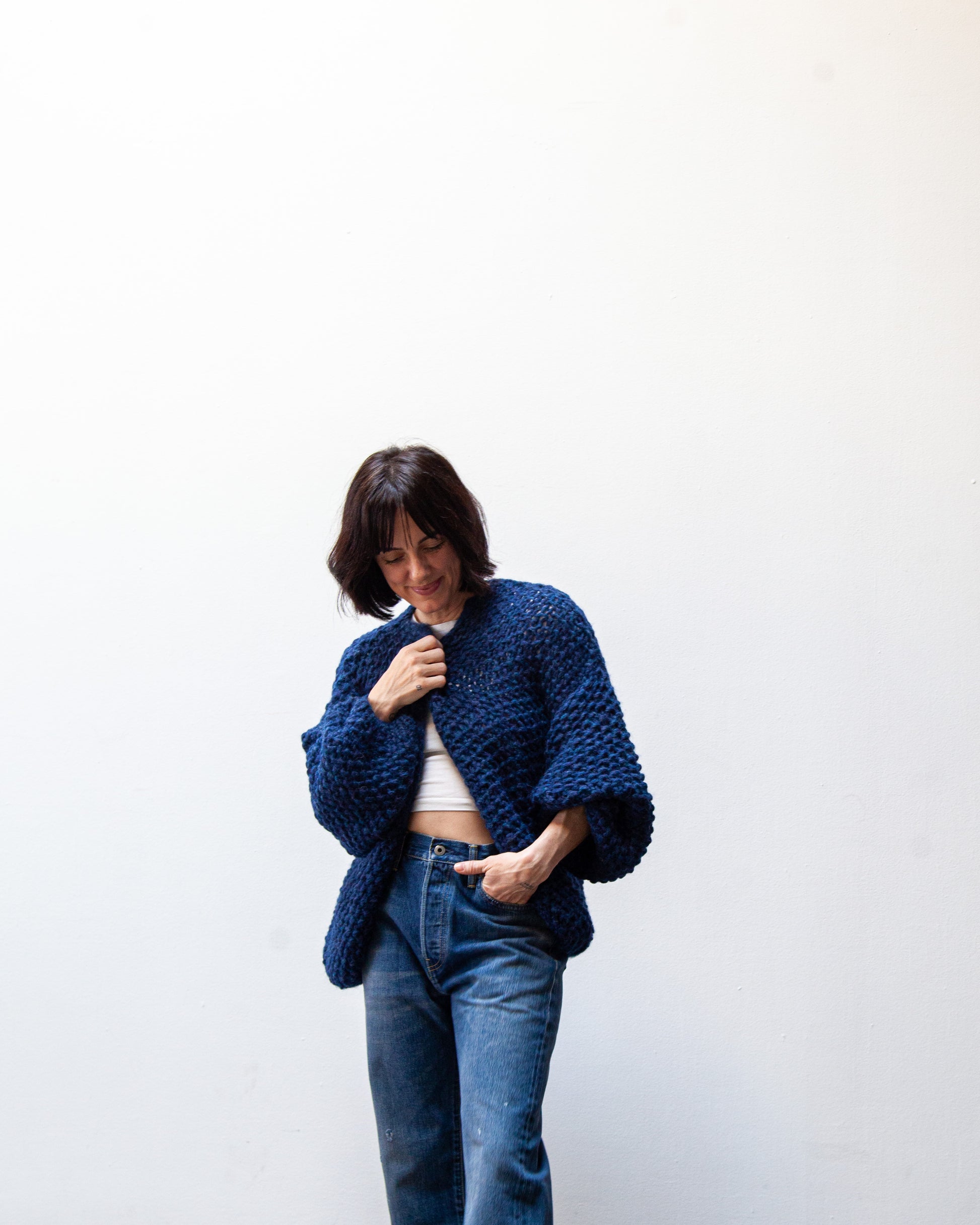 Person wearing a blue knitted sweater and jeans against a white background