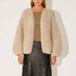 Woman wearing a beige textured cardigan over a green top and black leather skirt on a white background