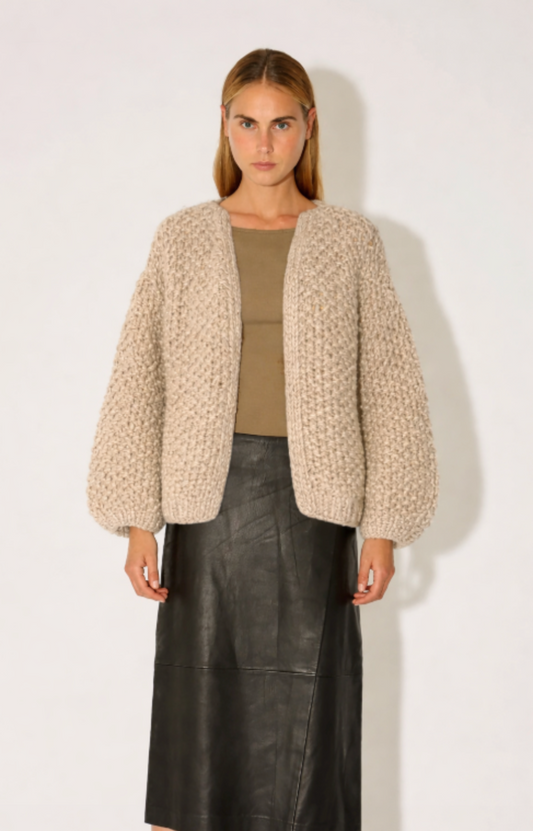 Woman wearing a beige textured cardigan over a green top and black leather skirt on a white background