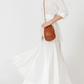 Person wearing a white dress holding a brown woven handbag on a white background