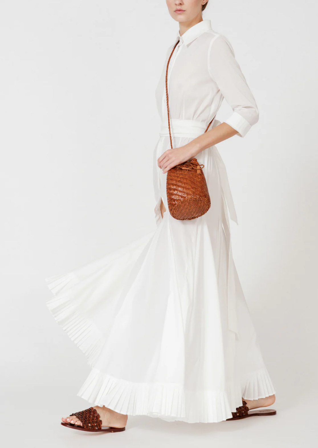 Person wearing a white dress holding a brown woven handbag on a white background