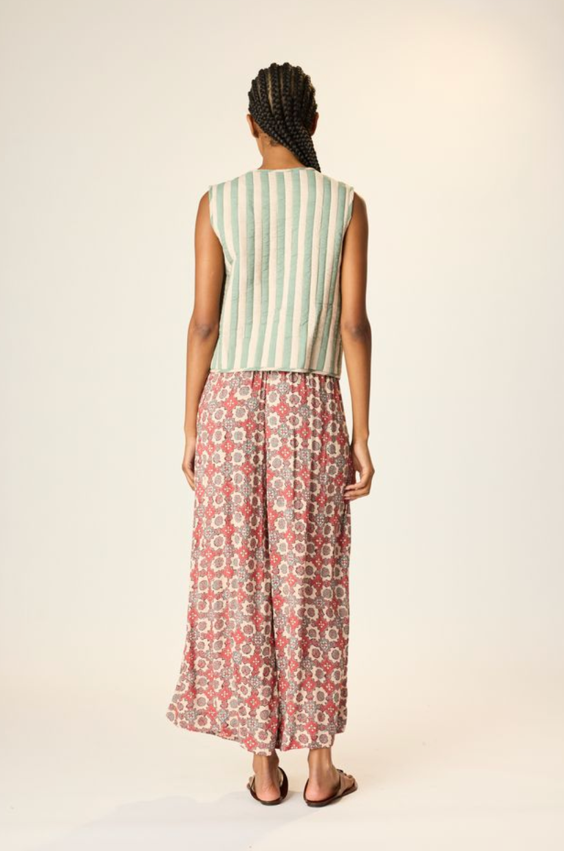Woman wearing a sleeveless striped top and patterned pants on a plain background