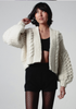 Person wearing a chunky knit cardigan over a black top and shorts on a plain background