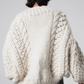 Person wearing a chunky knit sweater from behind on a plain background