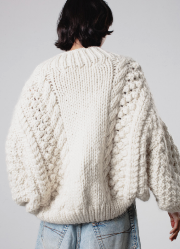 Person wearing a chunky knit sweater from behind on a plain background