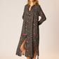 Woman wearing a black floral dress with a slit on a beige background