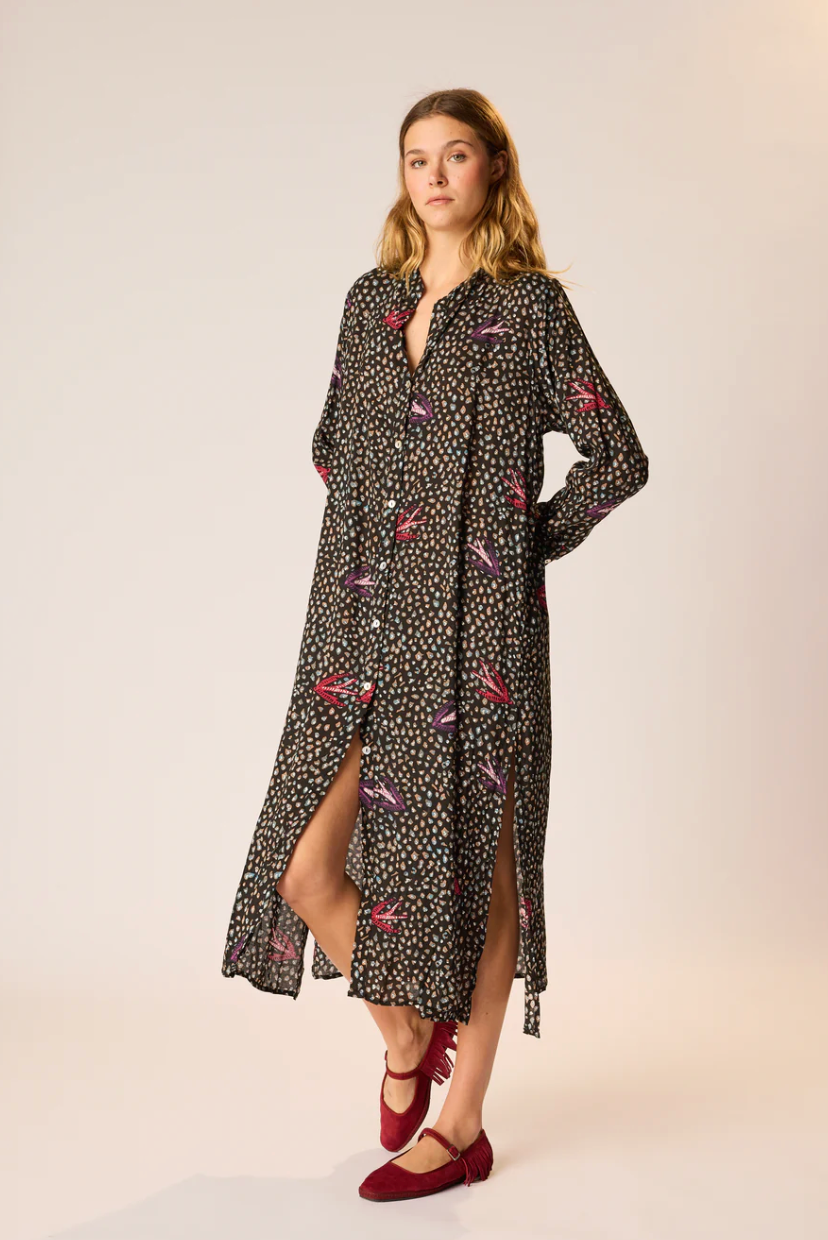 Woman wearing a black floral dress with a slit on a beige background