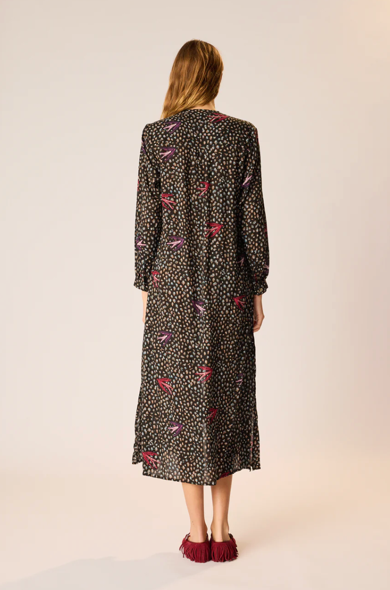 Woman wearing a long, dark dress with a pattern on a plain background