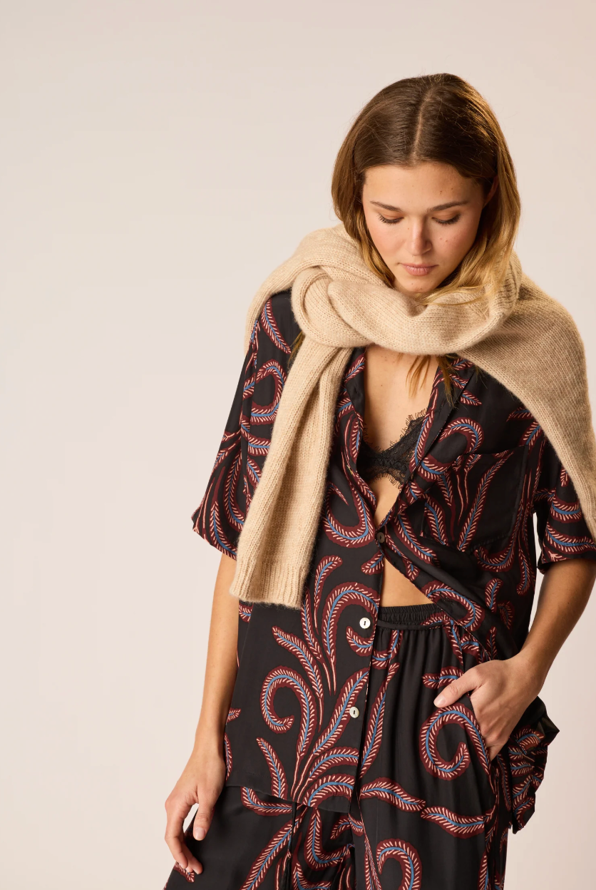 Woman wearing a patterned dress and beige scarf against a plain background