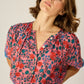 V-neck blouse with shell buttons. Short sleeves with button closure at cuff. Slightly pleated under collar to add body.