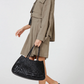 Woman holding a black woven handbag wearing a beige trench coat on a white background