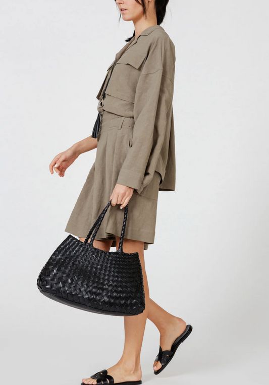 Woman holding a black woven handbag wearing a beige trench coat on a white background