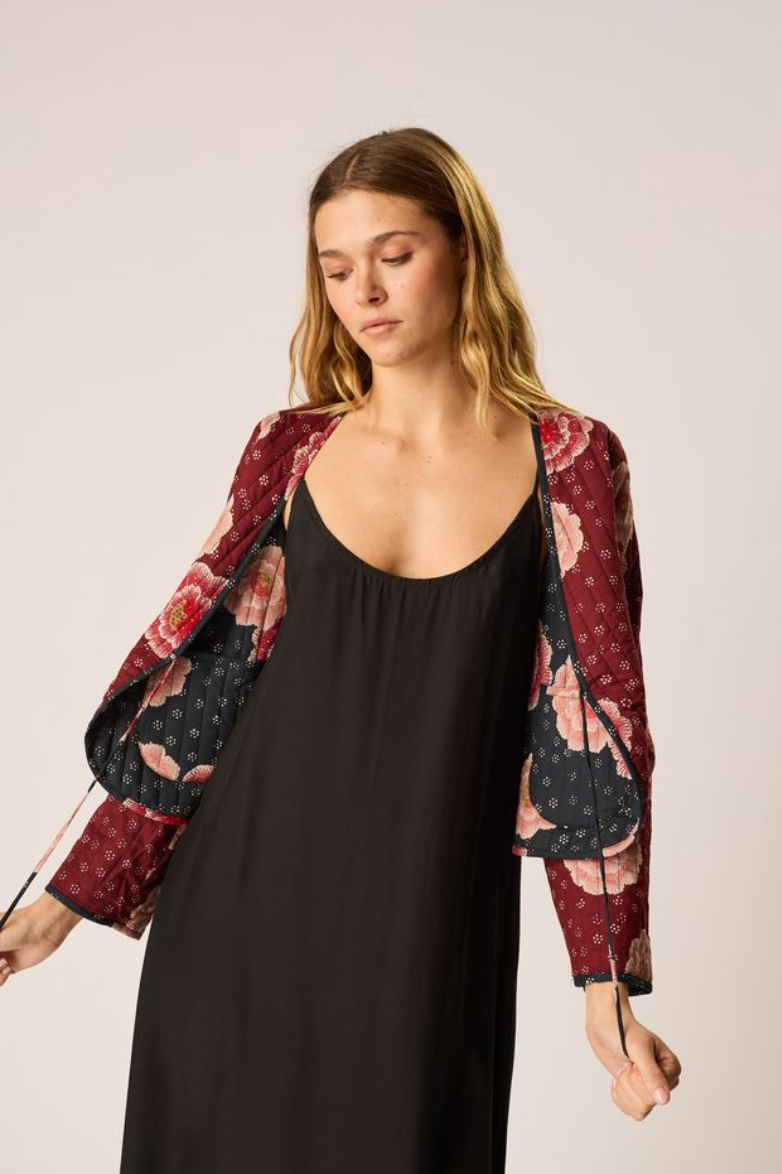 Woman wearing a black dress with a floral patterned jacket on a plain background